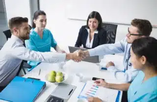 Healthcare professionals and financial advisors shaking hands during a meeting about medical facility loans and healthcare business financing solutions.