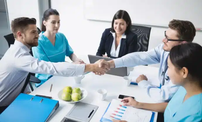Healthcare professionals and financial advisors shaking hands during a meeting about medical facility loans and healthcare business financing solutions.