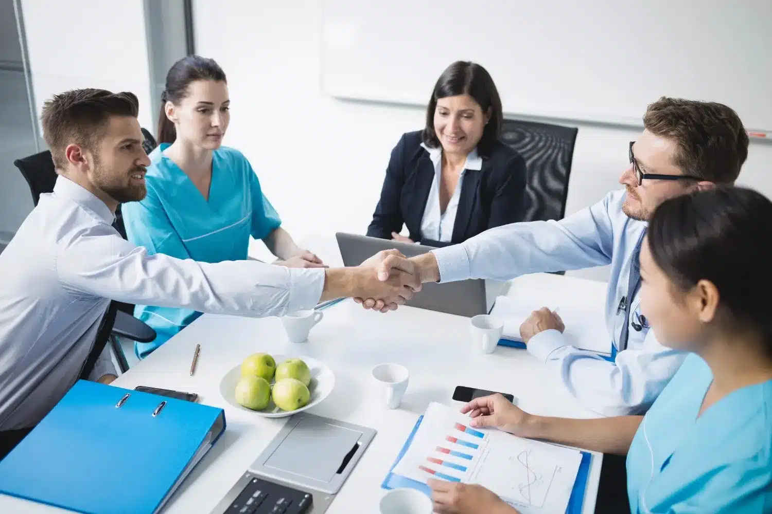 Healthcare professionals and financial advisors shaking hands during a meeting about medical facility loans and healthcare business financing solutions.